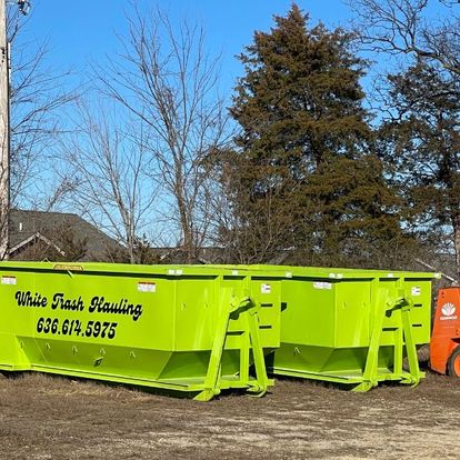 The image shows a truck from White Trash Hauling, a waste removal service. The truck is white with the company's logo and name displayed prominently on the side. It is parked outdoors on a clear day, surrounded by trees and grass. The truck is